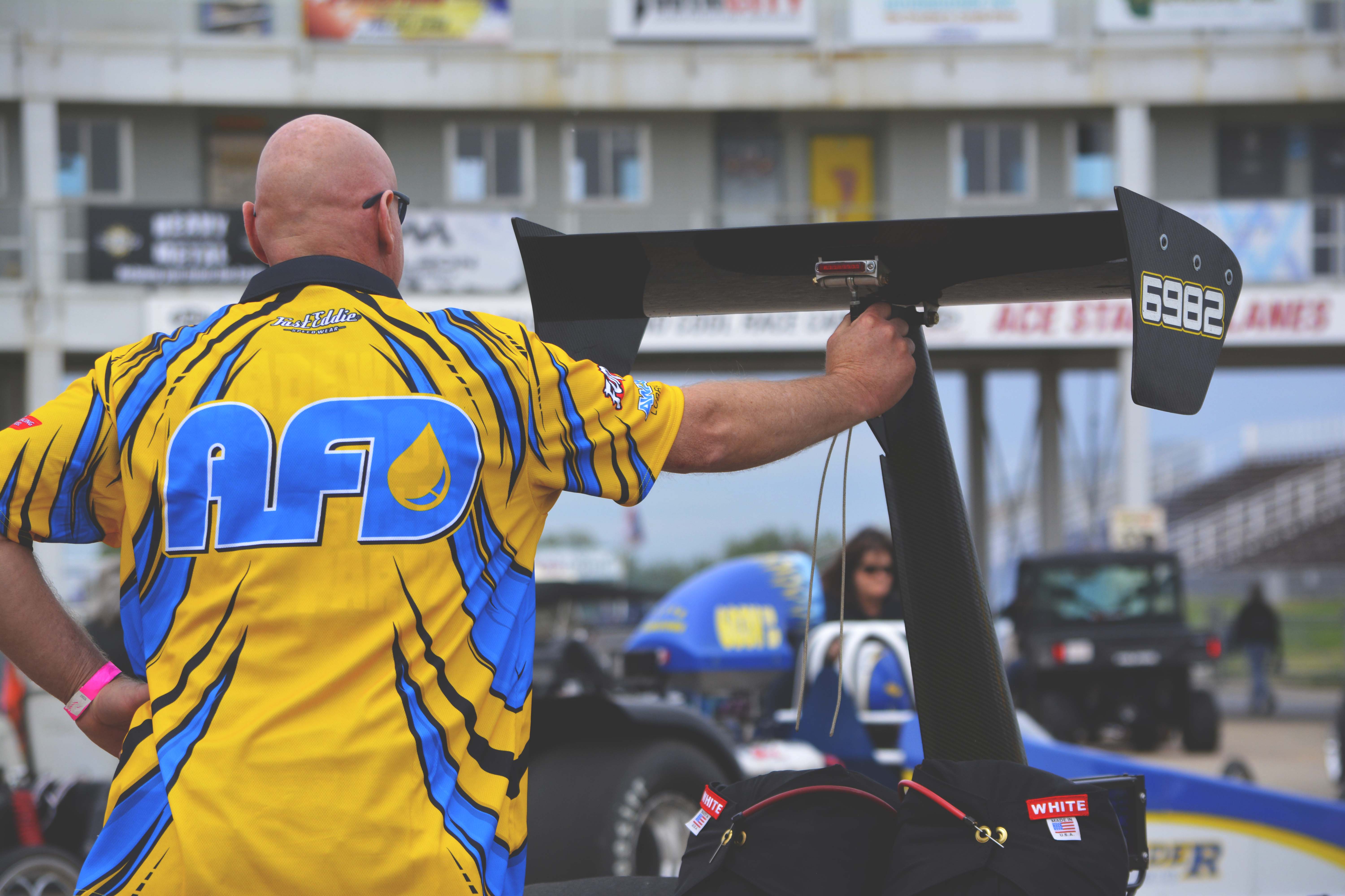 AFD crew member in team shirt leaning on the dragster rear wing at the racetrack