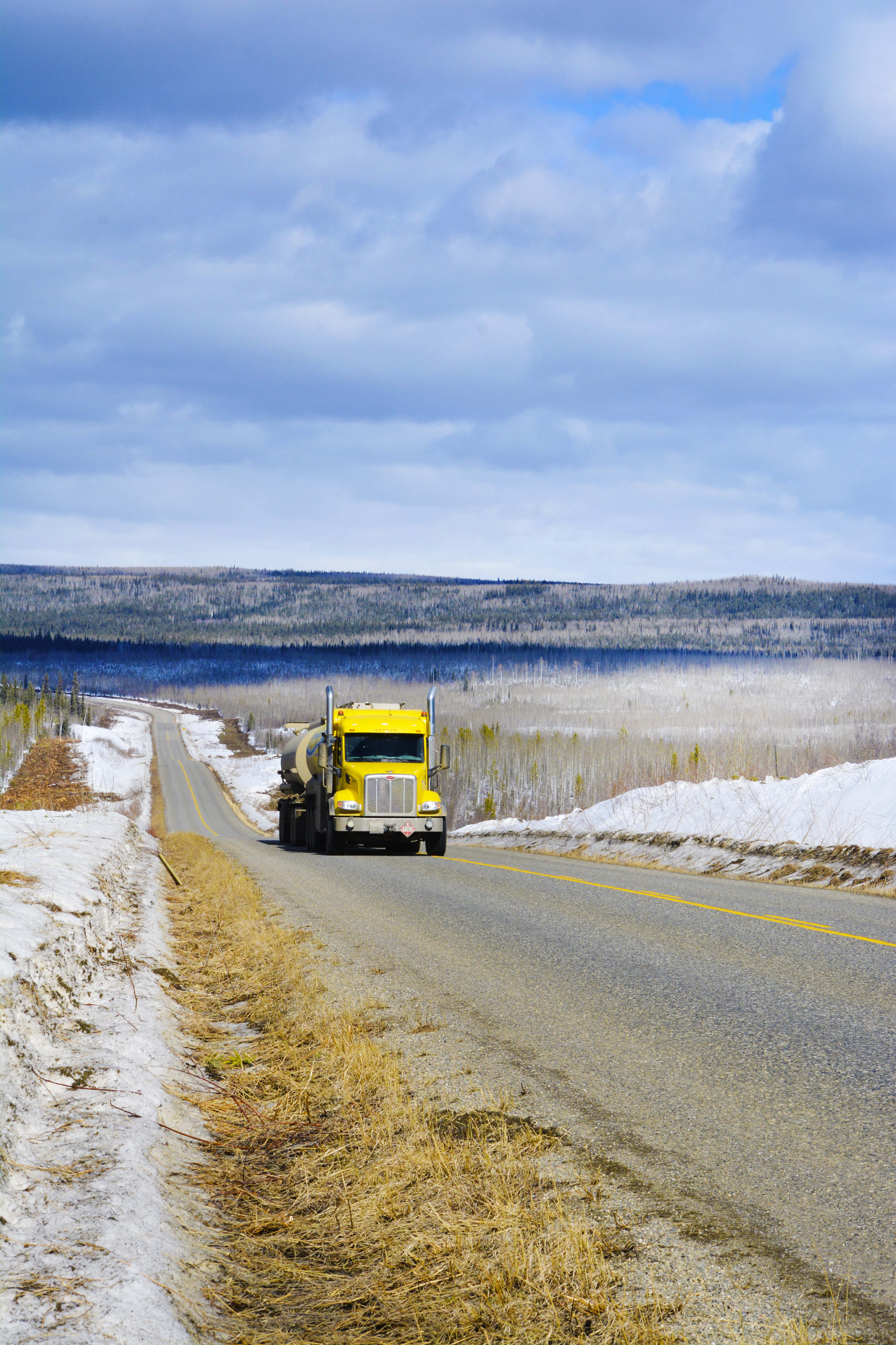 Yellow AFD Petroleum tanker truck driving on a rural Yukon road with snowy fields and mountains