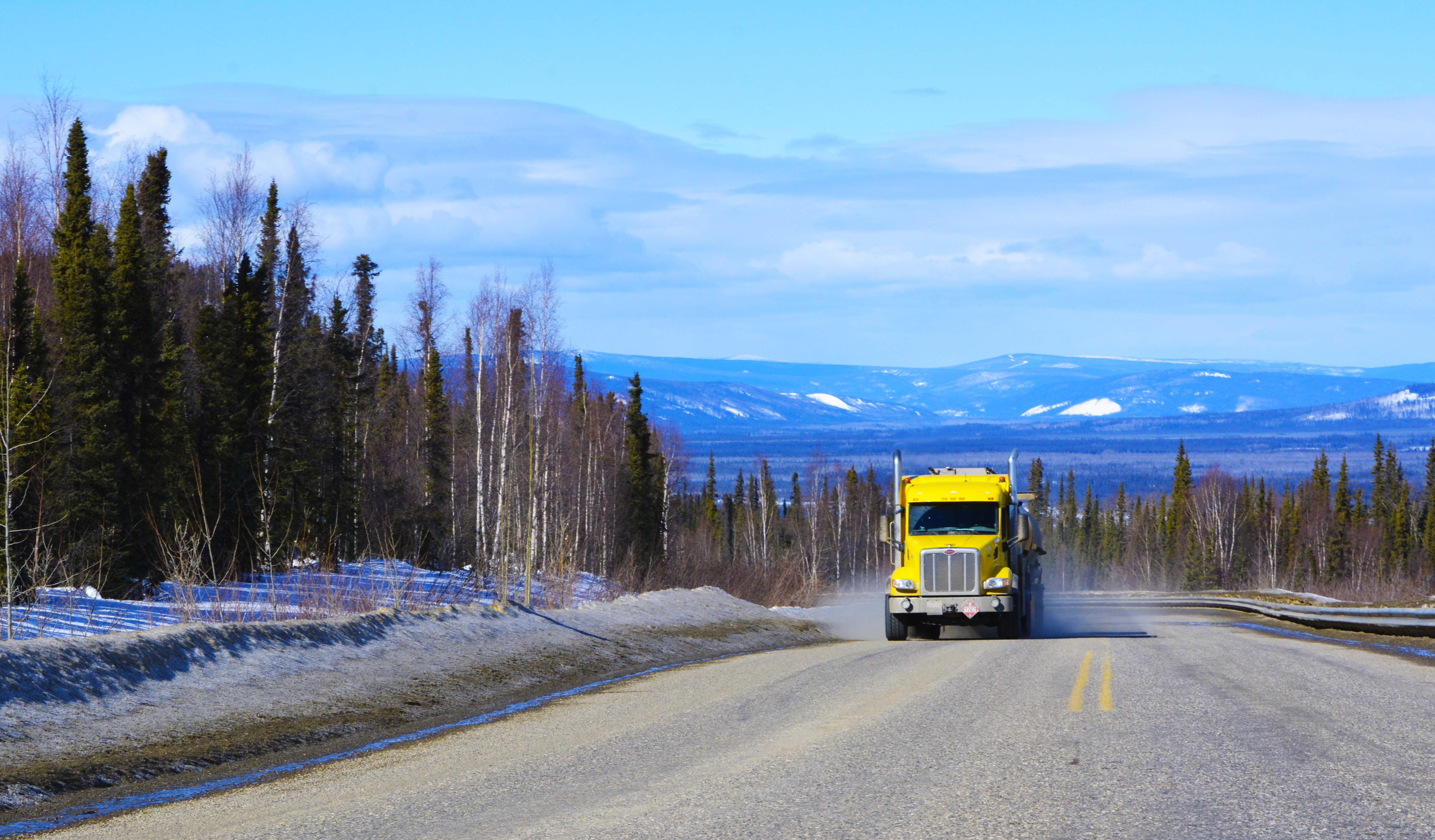 Yellow AFD Petroleum tanker truck driving toward the viewer on a highway through snowy Yukon mountains