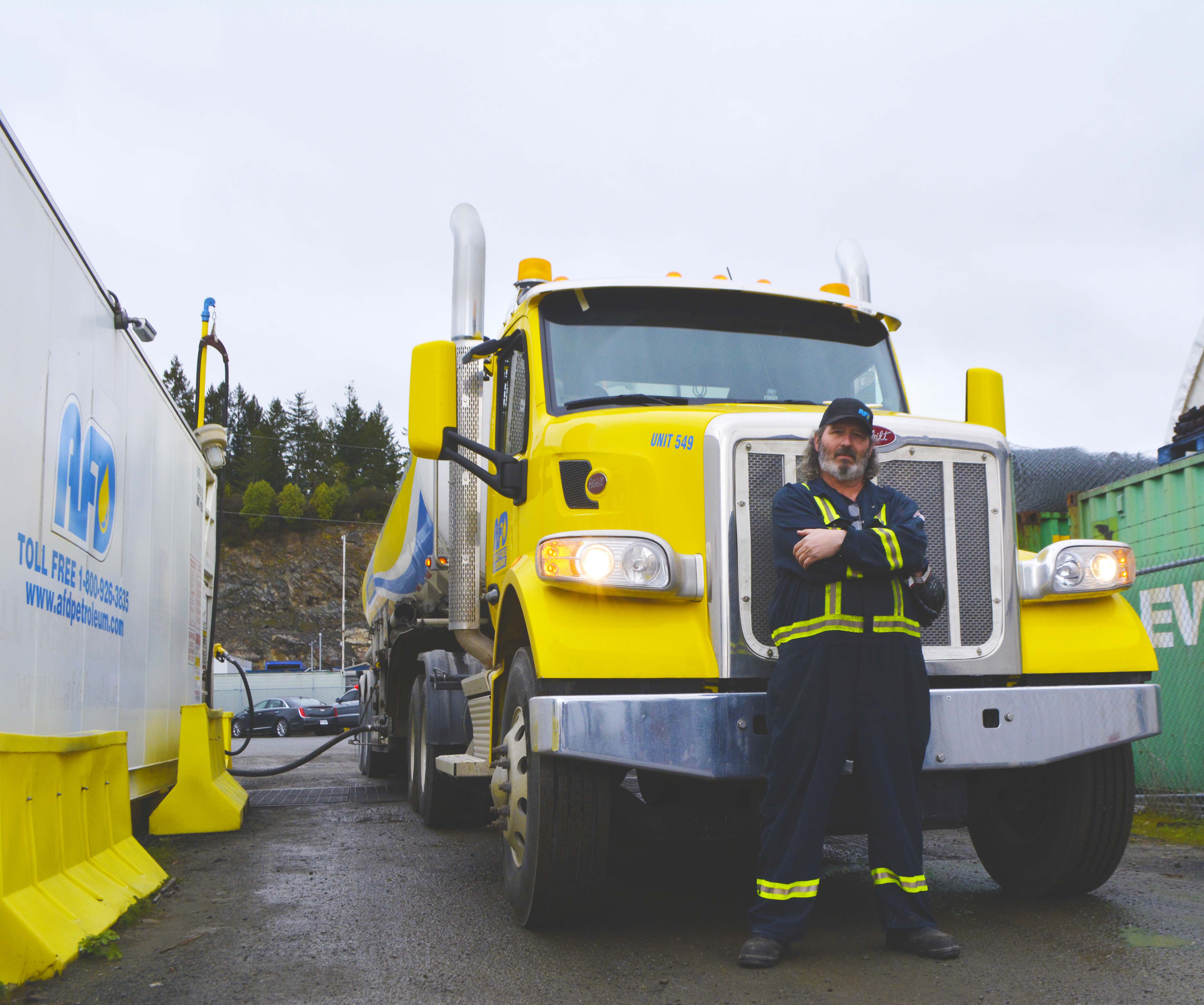 AFD Petroleum employee in high-visibility coveralls standing with arms crossed in front of a yellow tanker truck at the Victoria site