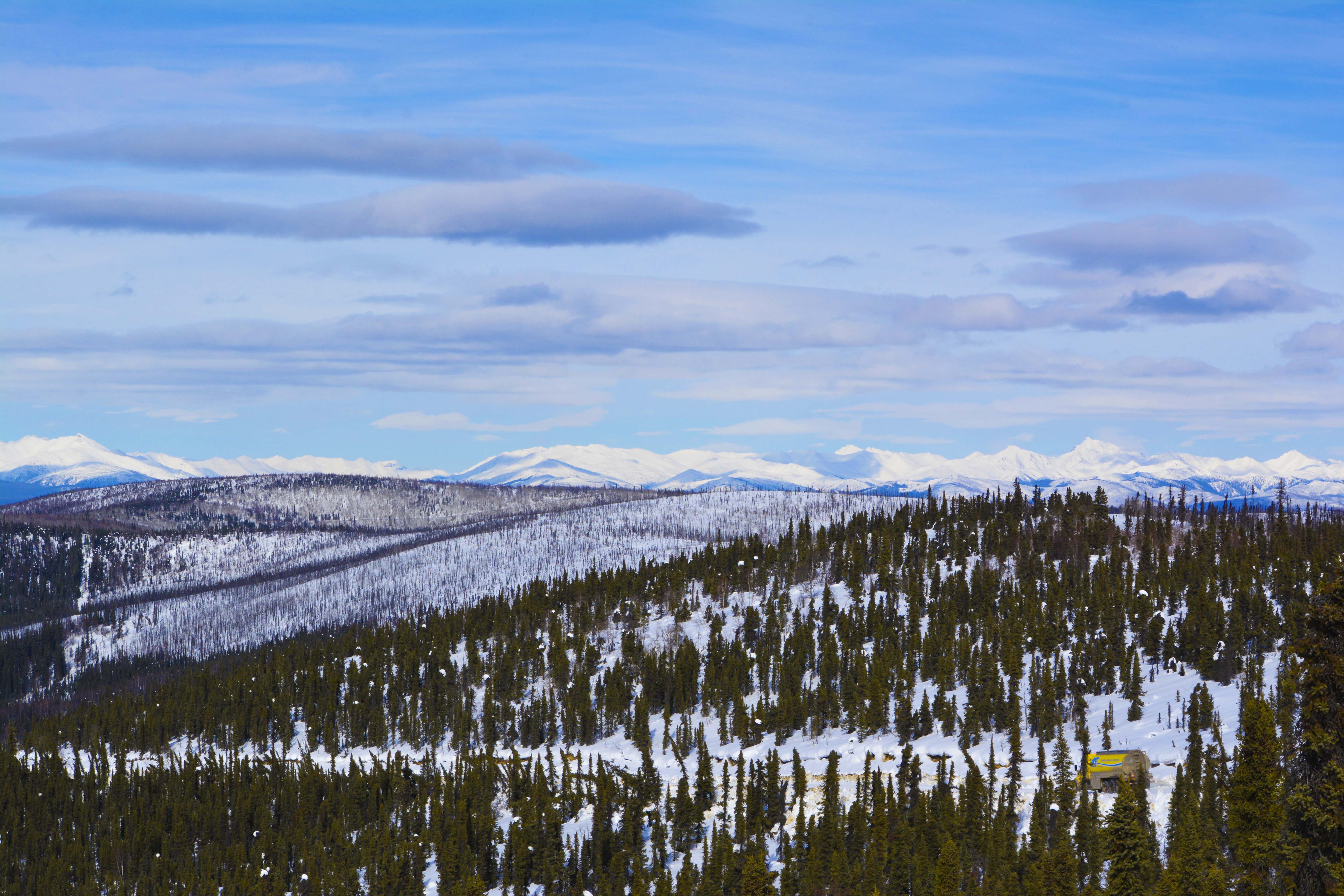 Panoramic winter landscape in the Yukon with a small AFD fuel truck on a road through snowy forest and mountains