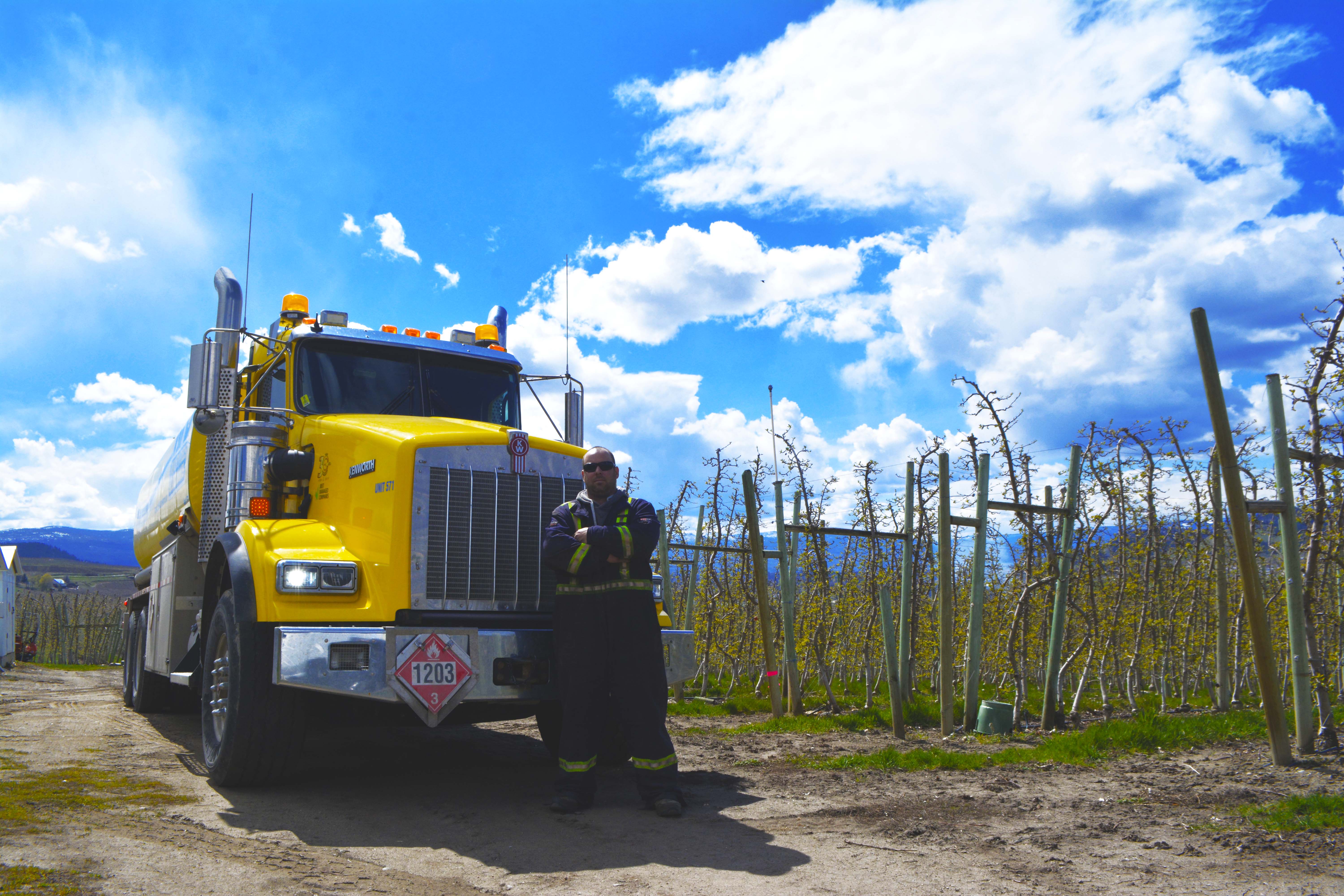 AFD Petroleum crew member in high-visibility coveralls standing in front of the yellow fuel tanker at an orchard
