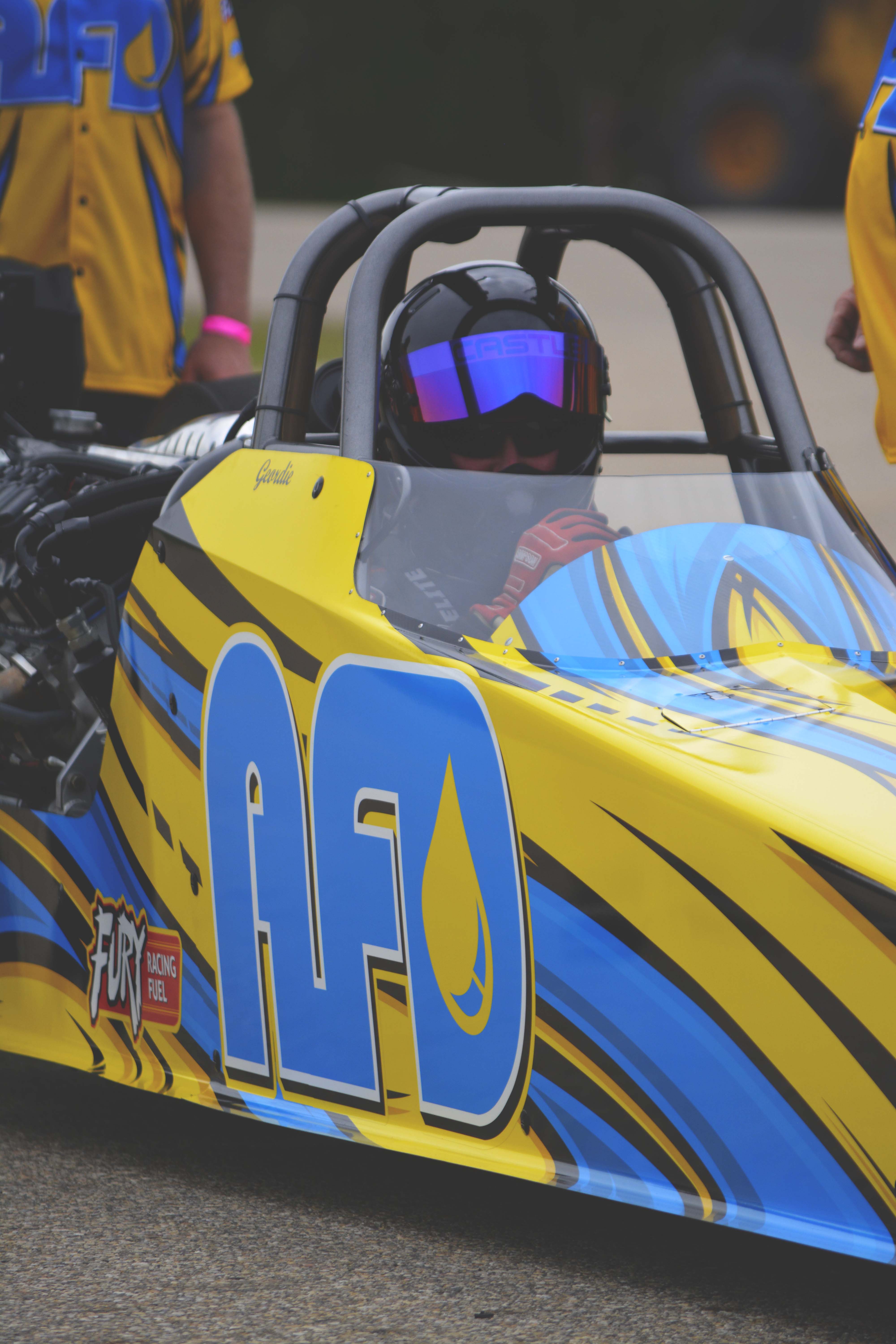 AFD dragster driver in cockpit wearing helmet with reflective visor and red racing gloves