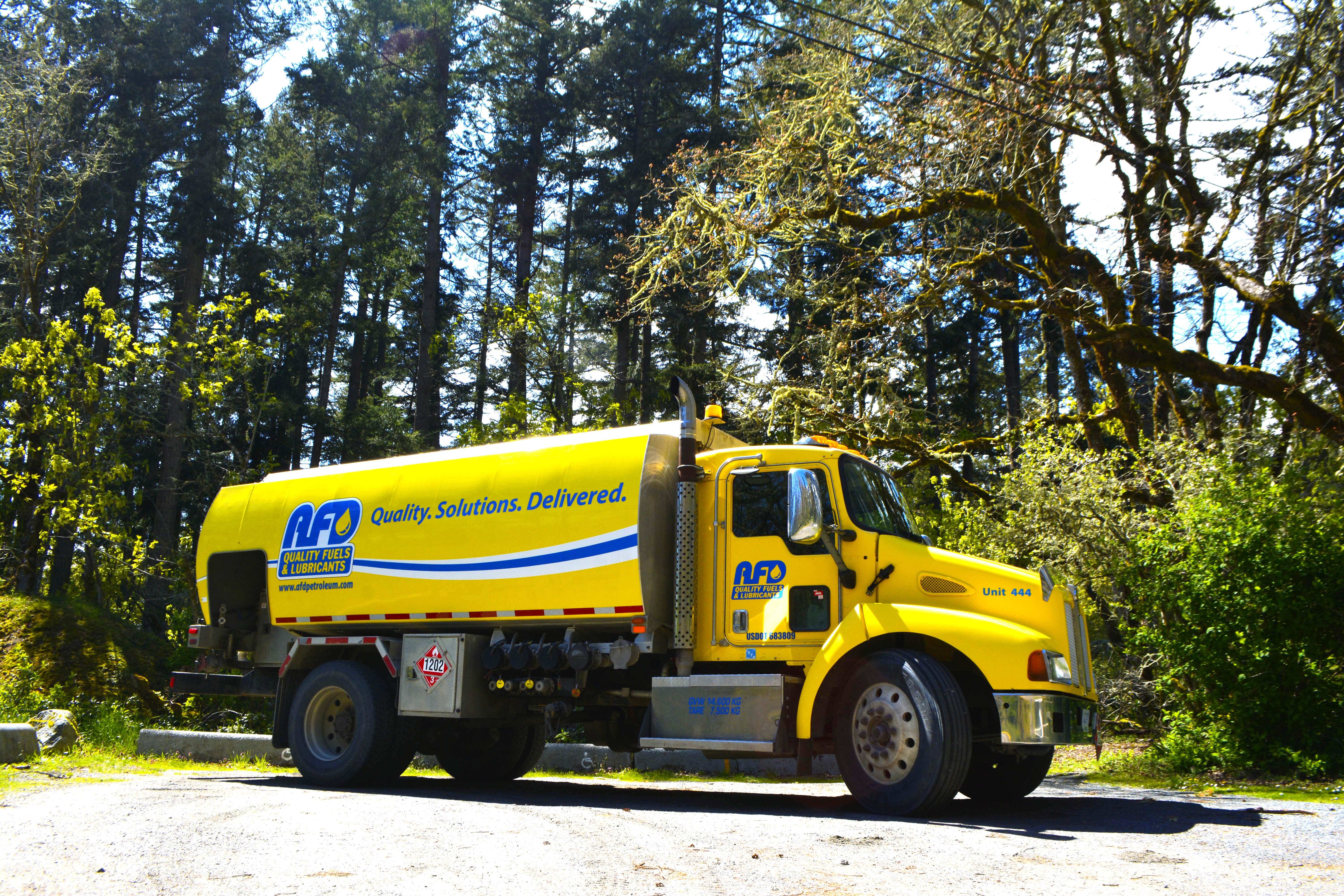 Yellow AFD Petroleum fuel truck in profile parked on gravel among tall trees at the Victoria site
