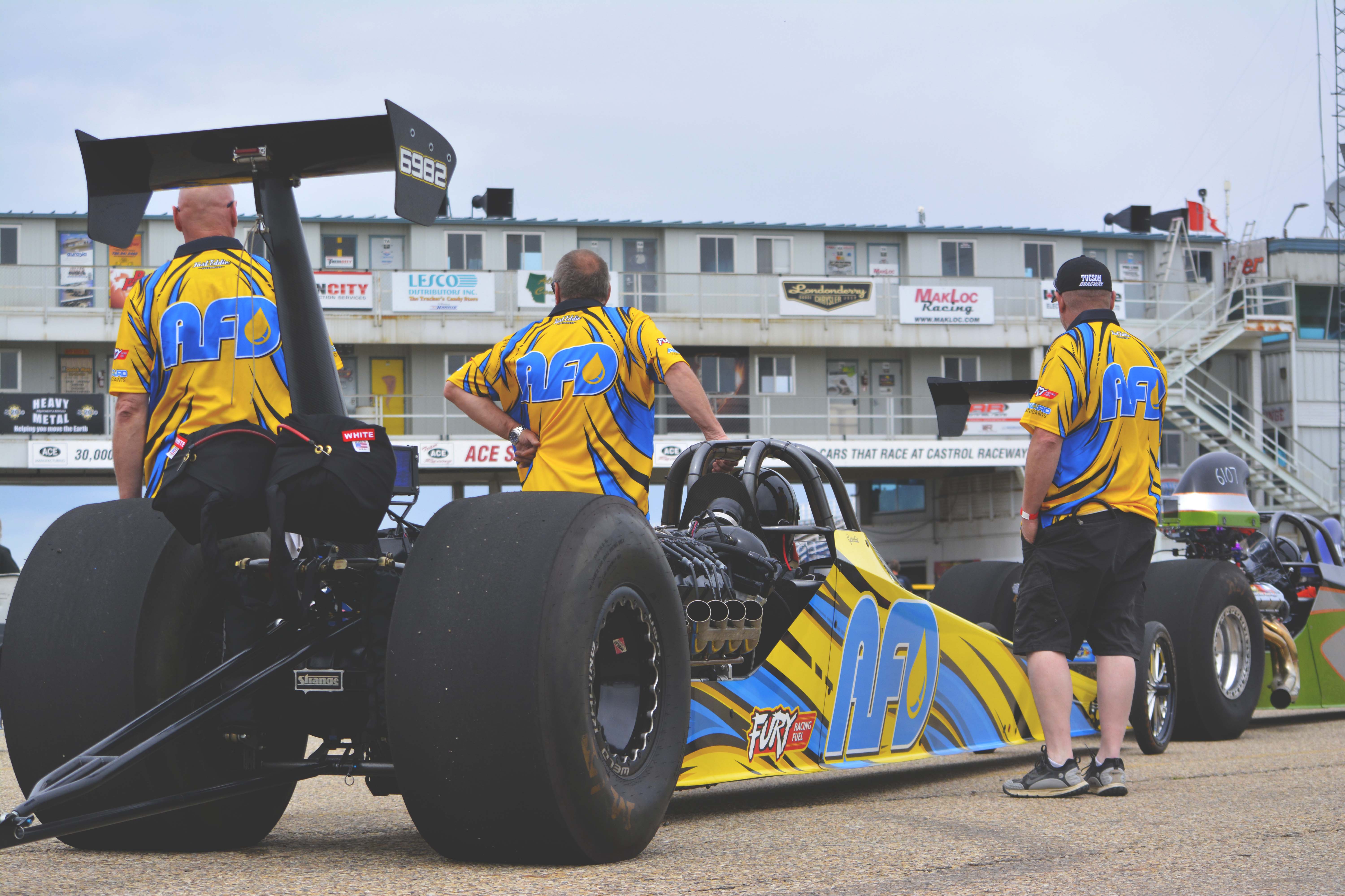 AFD dragster staged at Castrol Raceway with crew members in team shirts