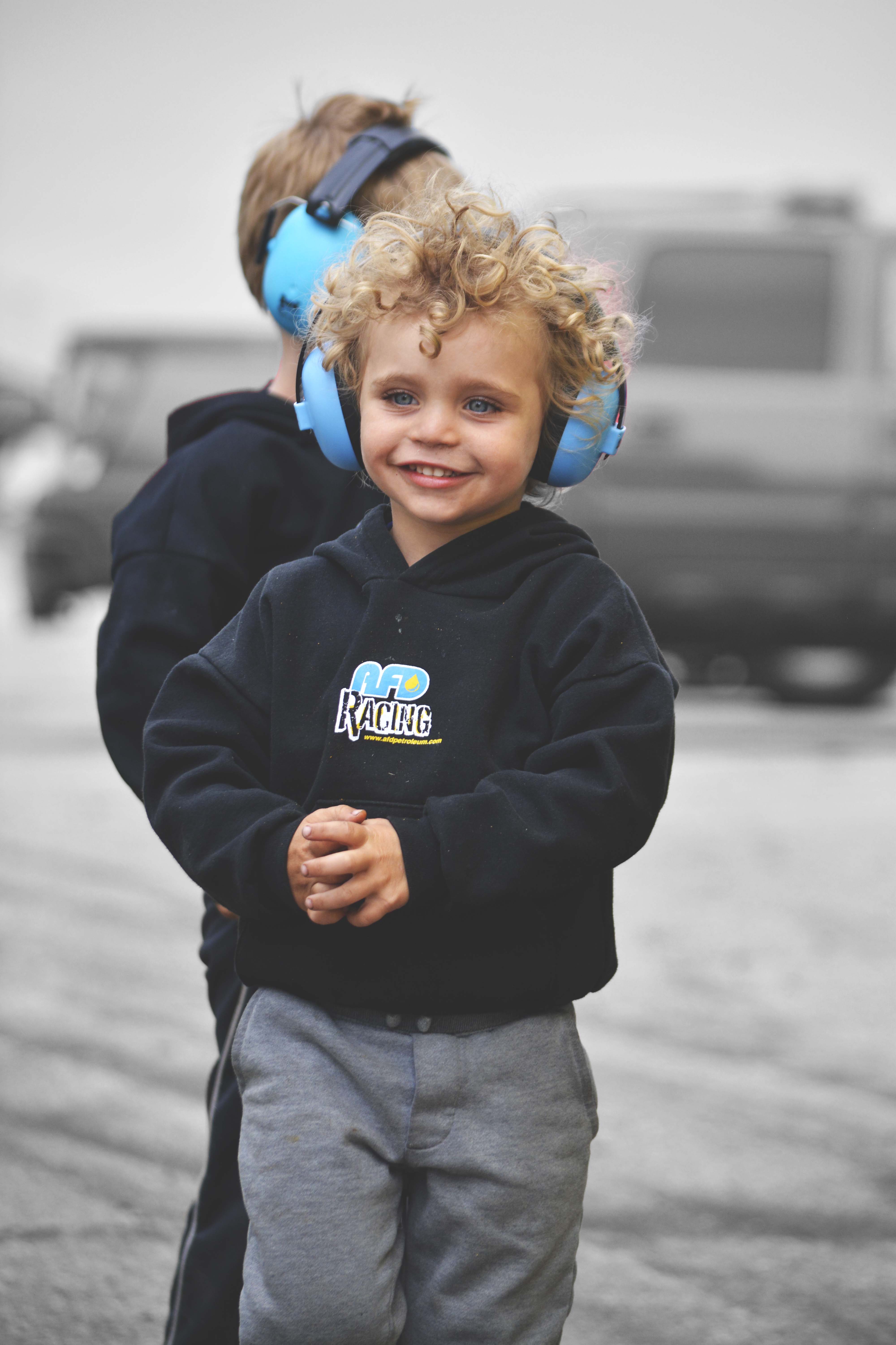 Child in AFD Racing hoodie and ear protection smiling at the camera at the drag racing event