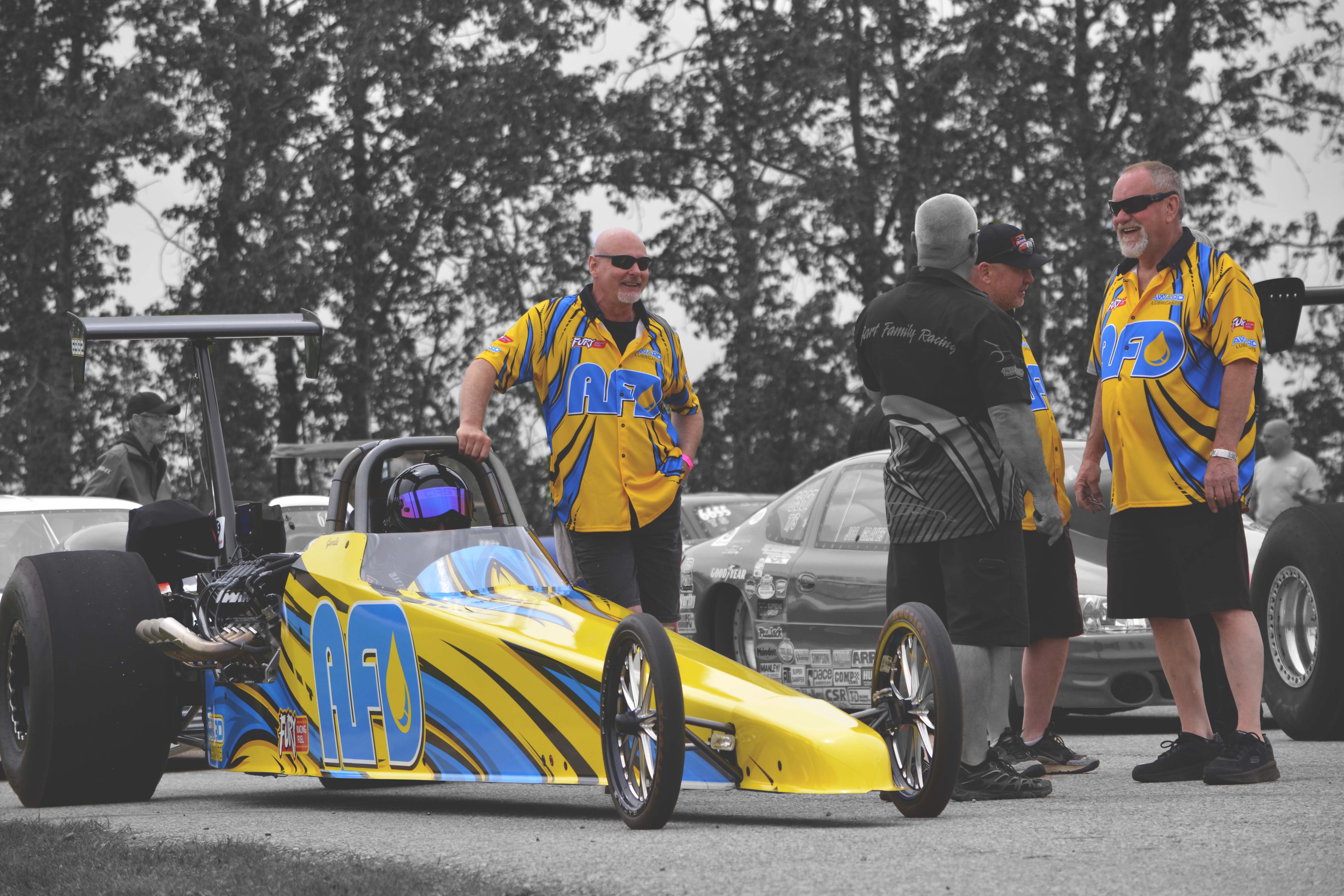 AFD Petroleum racing team posing with their yellow dragster at the track