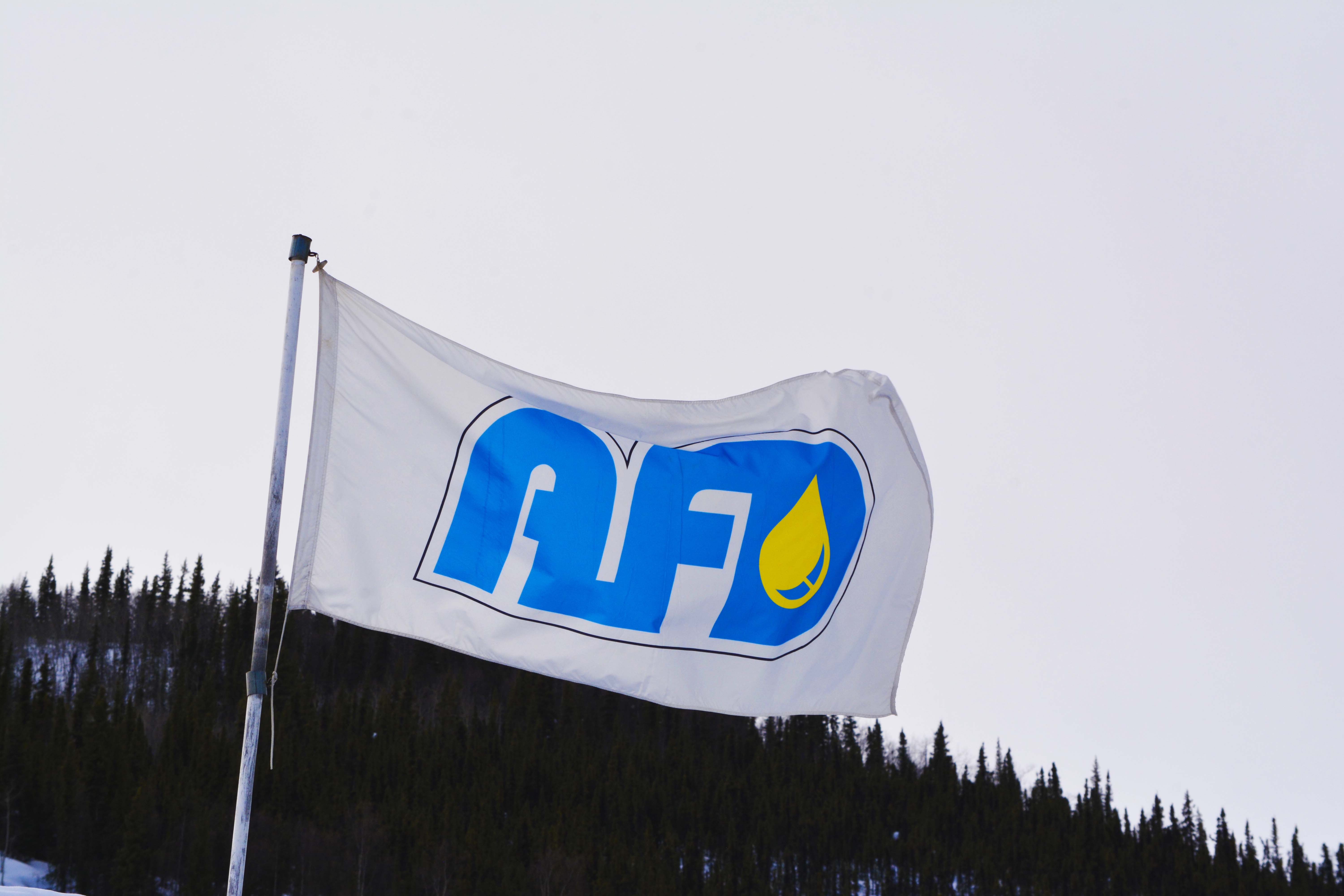 White AFD Petroleum flag with the blue and yellow logo waving against an overcast Yukon sky