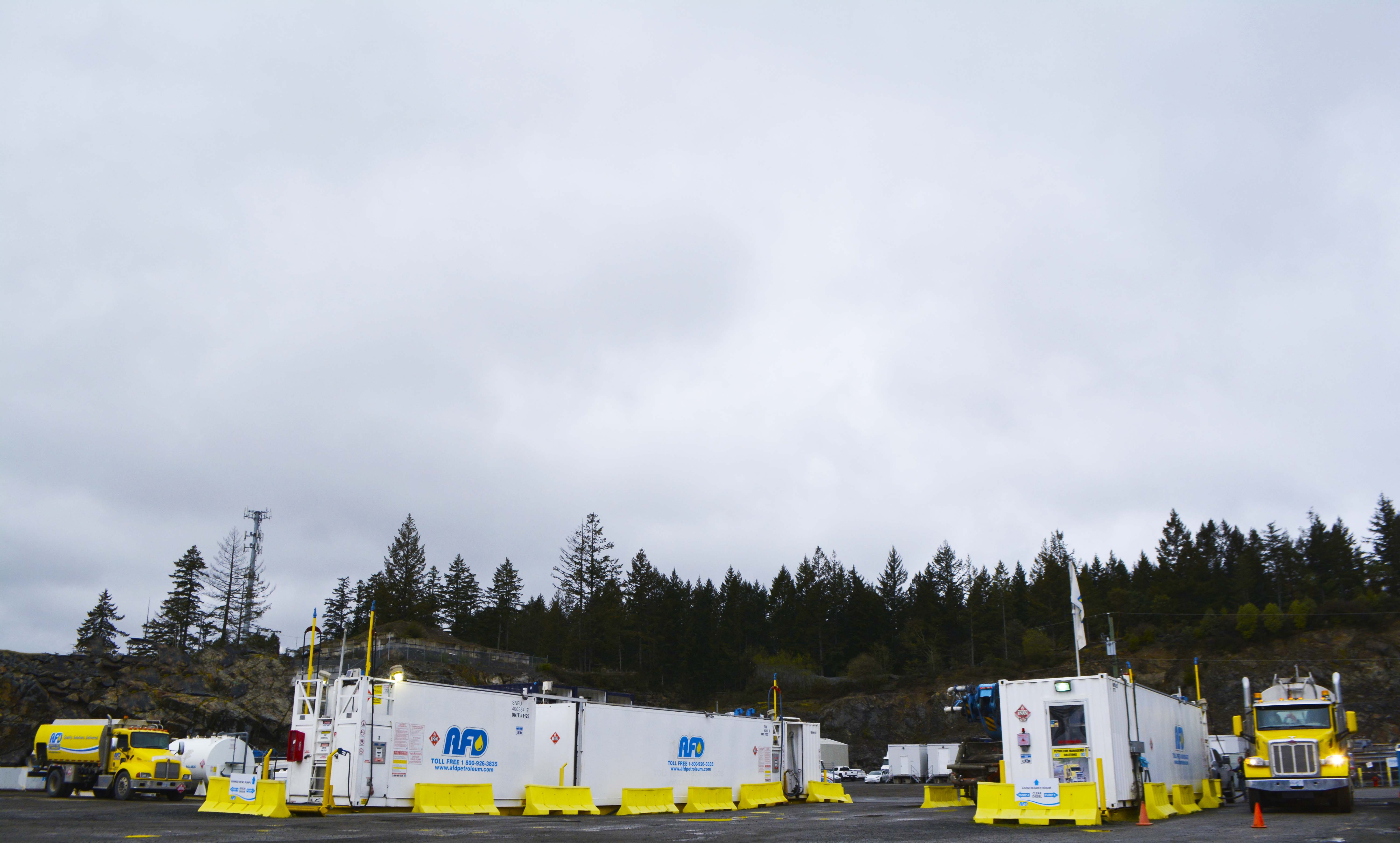 Wide view of the AFD Petroleum Victoria job site with white storage units, yellow barriers and a forested cliff behind