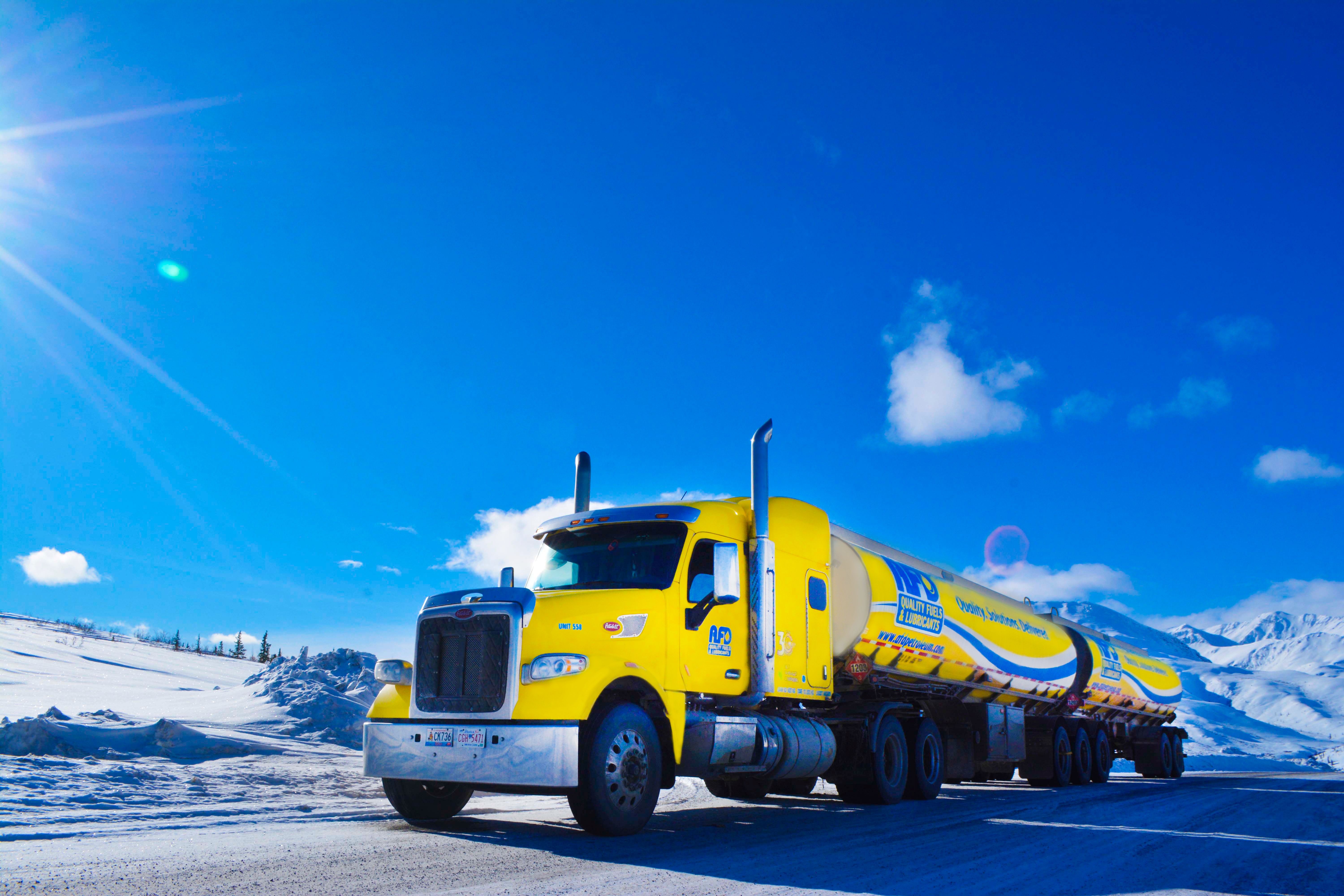 Yellow AFD Petroleum fuel tanker driving on a snow-covered road under a clear blue sky in the Yukon