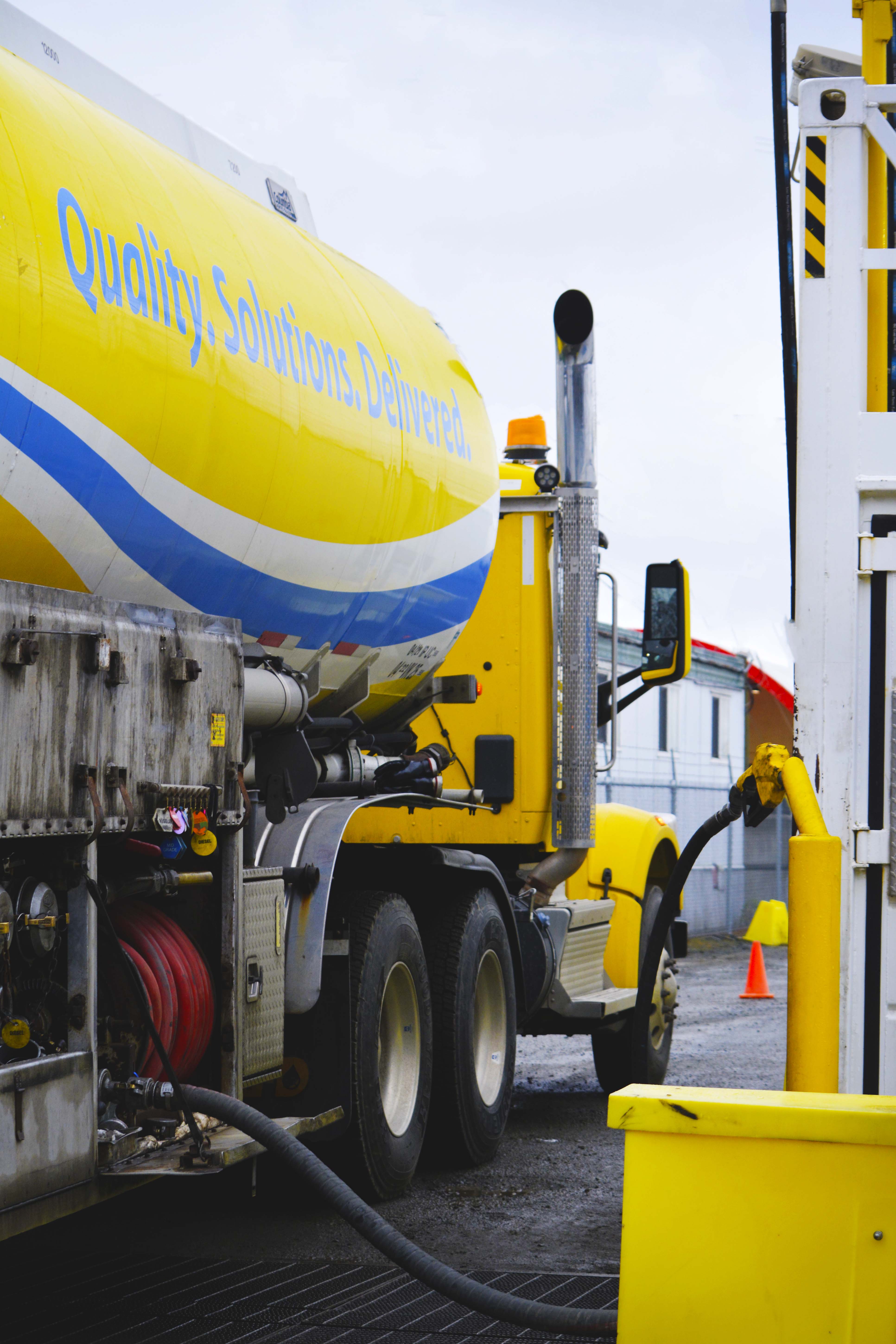 Vertical detail shot of an AFD Petroleum fuel truck being refueled with a yellow pump and red hoses