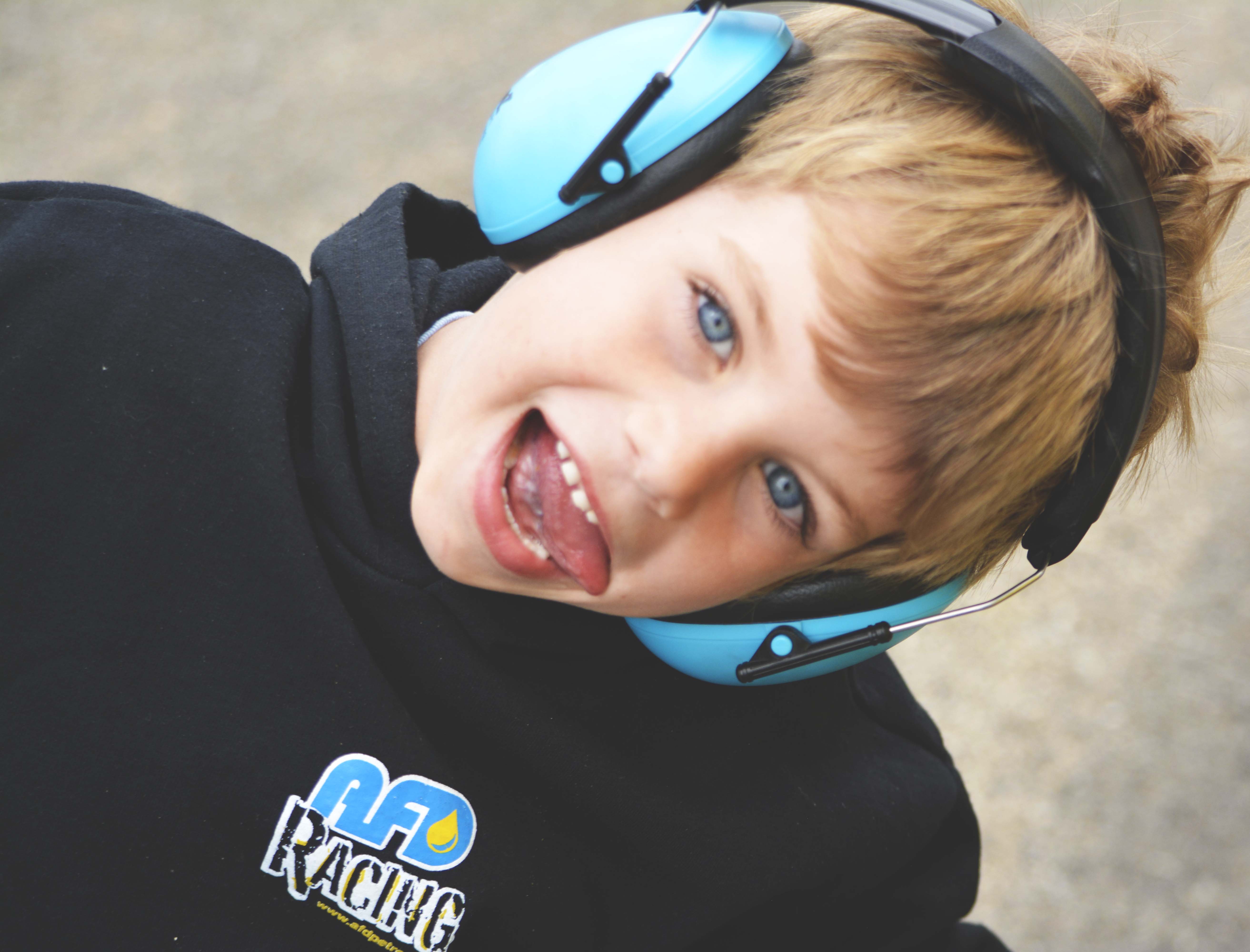 Young boy in AFD Racing hoodie and blue ear protection smiling and sticking his tongue out