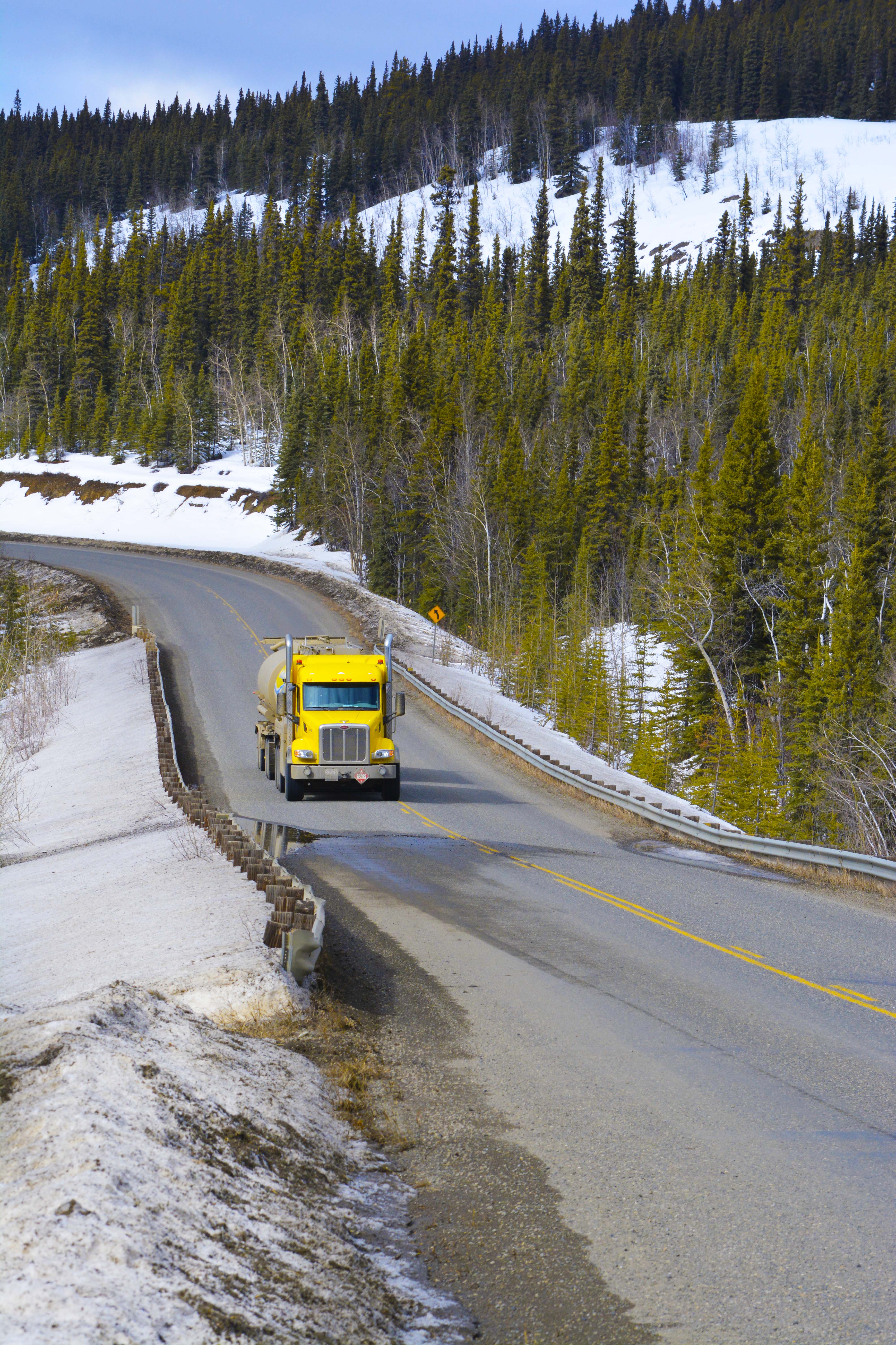 Vertical shot of a yellow AFD tanker truck navigating a curving snowy road through evergreen forest