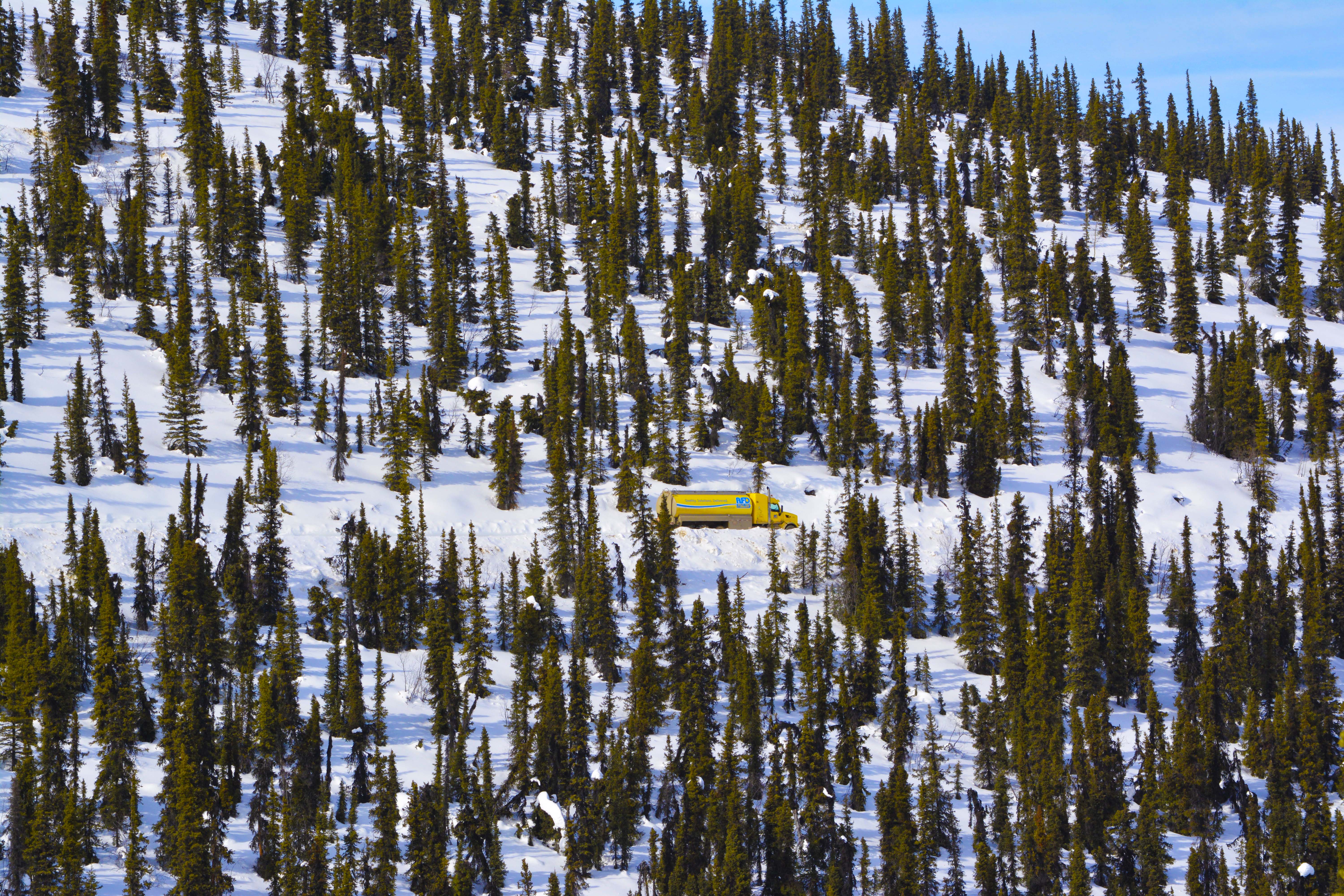 Aerial view of a single yellow AFD Petroleum tanker truck in a snowy forest clearing in the Yukon