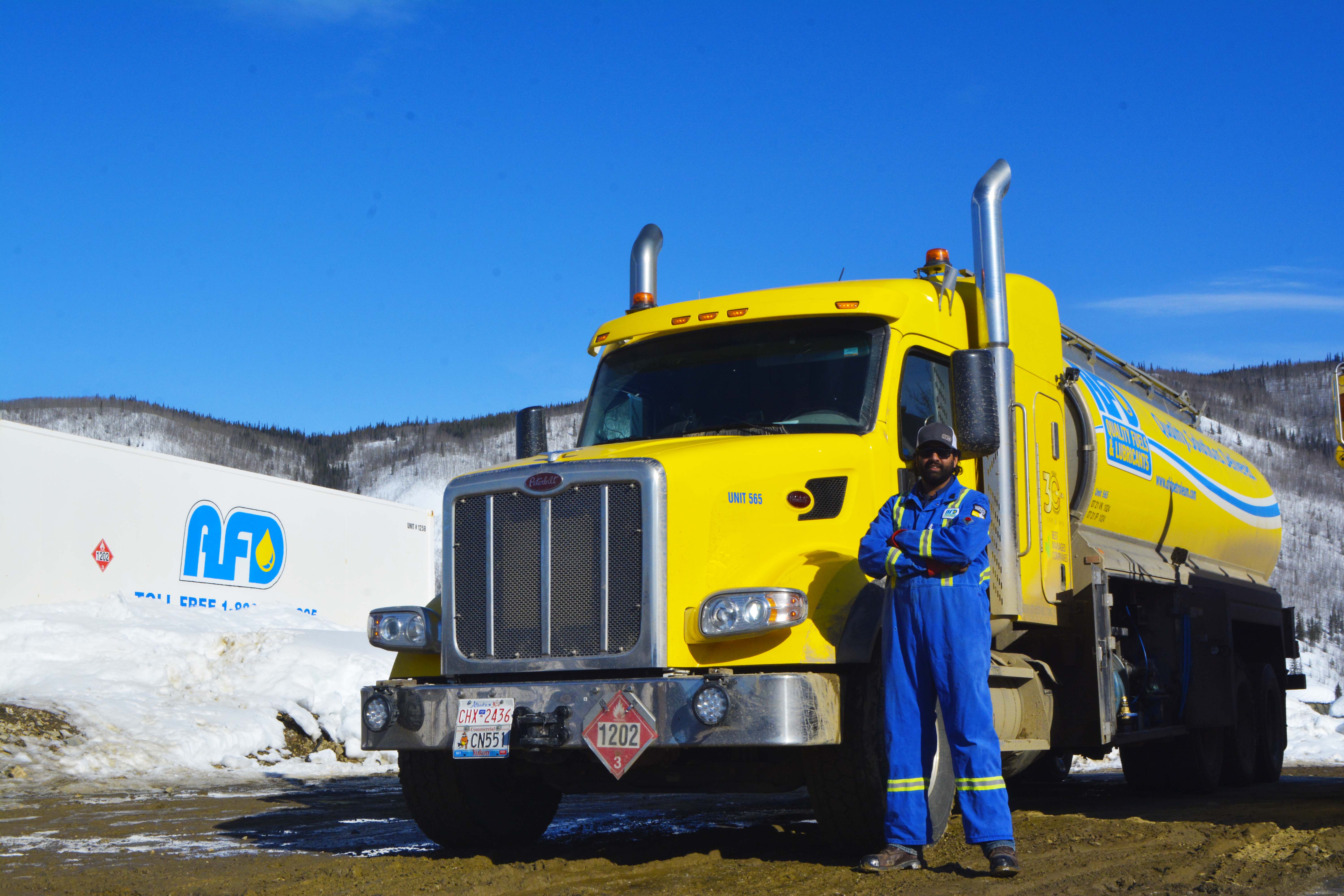 AFD Petroleum worker in blue coveralls with arms crossed in front of a yellow tanker truck in the Yukon