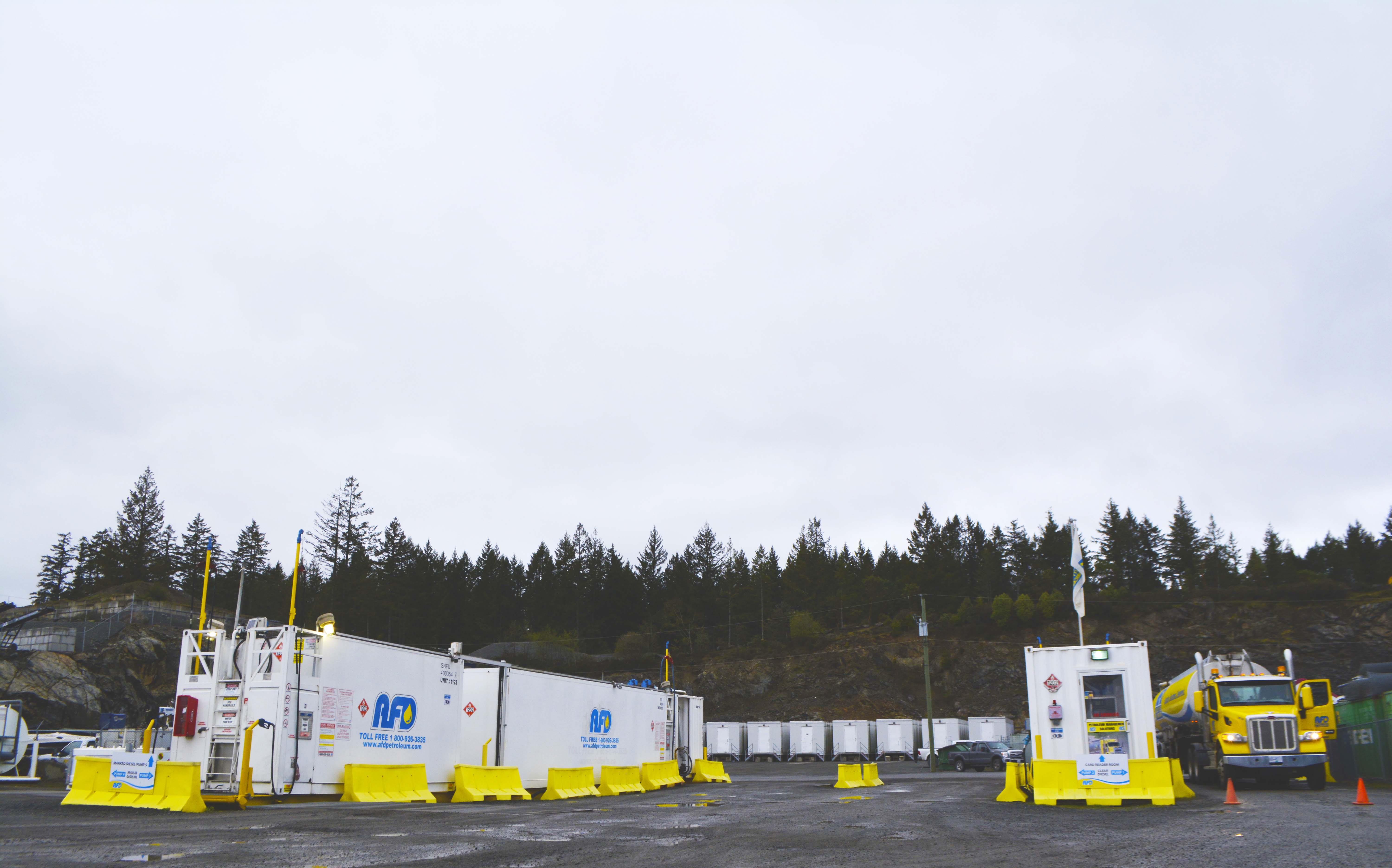 High-angle view of the AFD Petroleum Victoria yard with white office trailers and fuel units below a rocky treed slope
