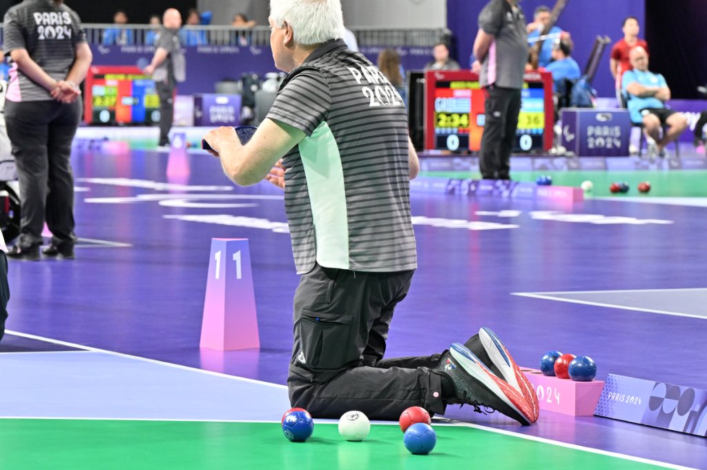 Referee kneeling on the Boccia court examining ball positions at Paris 2024