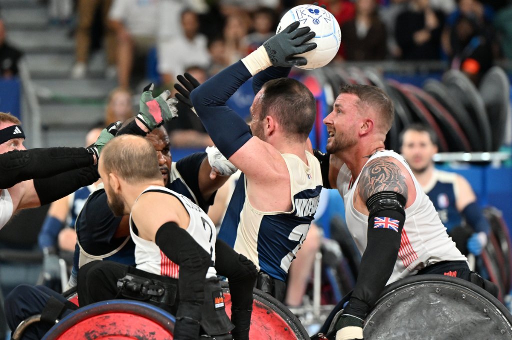 Great Britain wheelchair rugby player raises ball above French defenders during GBR vs FRA match