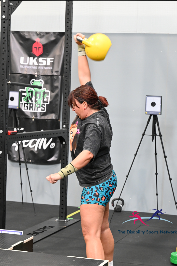 Athlete pressing a yellow kettlebell overhead inside the gym rig at Alt Movement