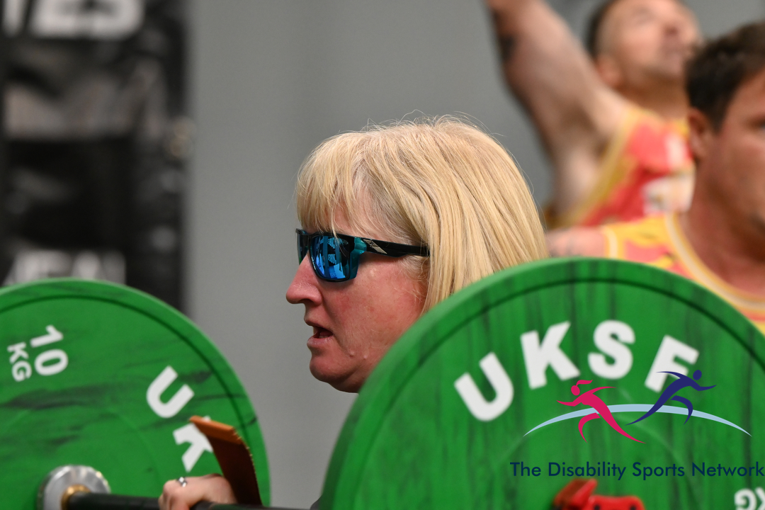 Athlete wearing blue-tinted sunglasses holding a barbell loaded with green UKSF plates at Alt Movement