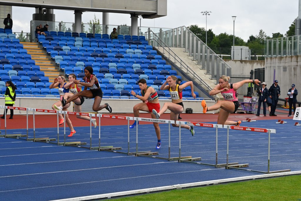 Six athletes clearing hurdles together at Birmingham Alexander Stadium