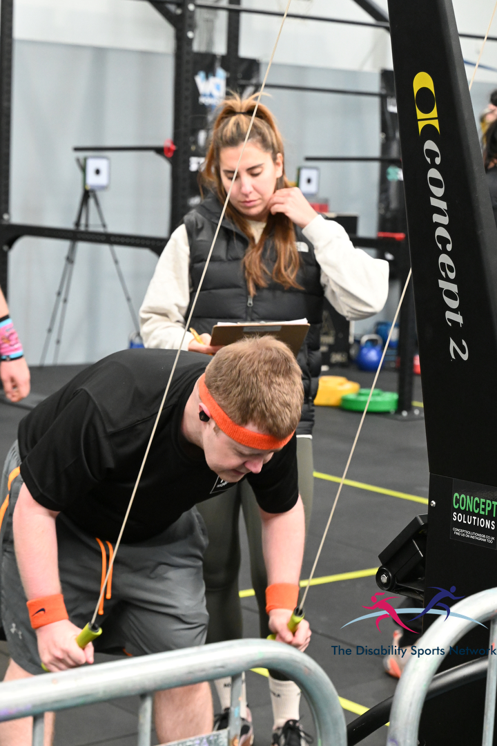 Athlete rowing on a Concept2 machine while a coach with a clipboard observes at Alt Movement