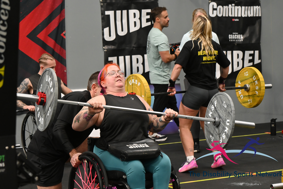 Wheelchair athlete lifting a barbell with a spotter assisting at Alt Movement