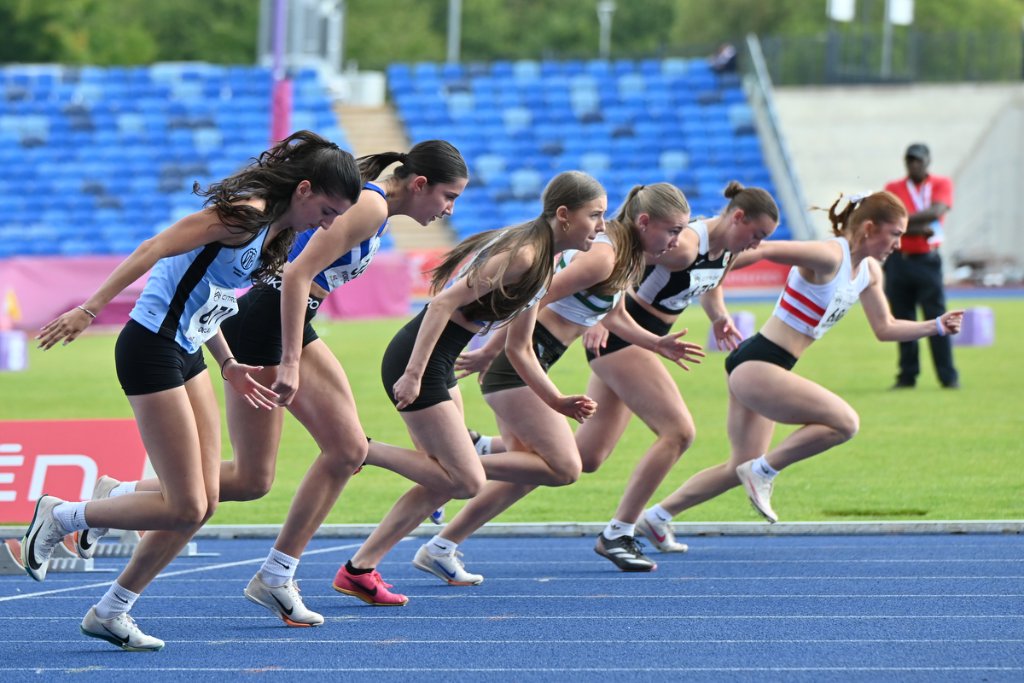 Young female athlete in yellow Nike kit clearing a hurdle