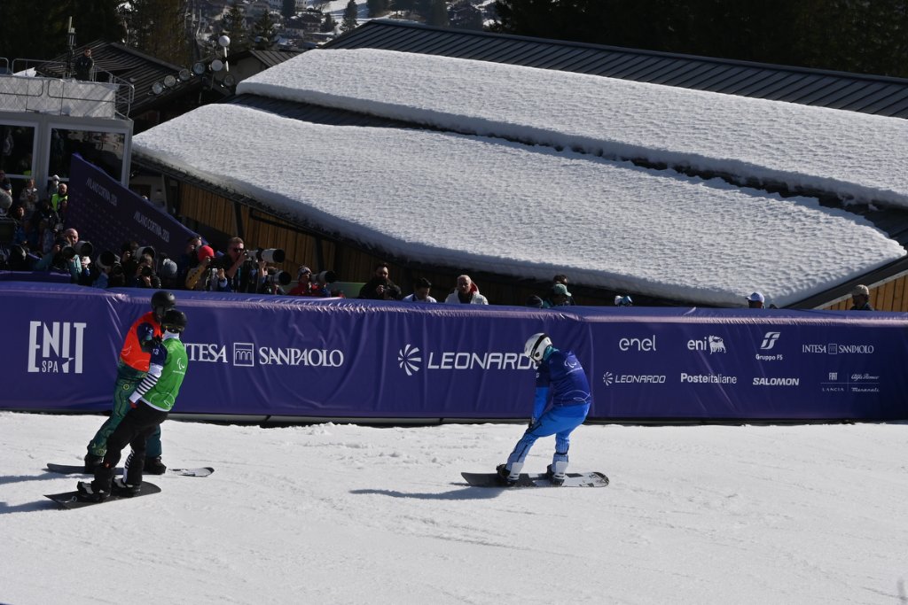 Two para snowboarders crossing the finish line with spectators watching at Milan Cortina 2026