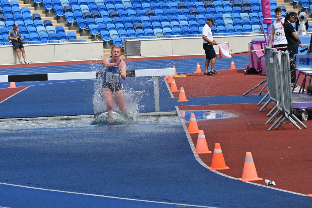 Female steeplechase athlete splashing through the water jump