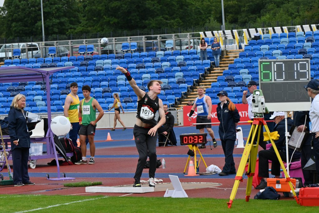 Shot put athlete #1017 releasing the shot with scoreboard visible