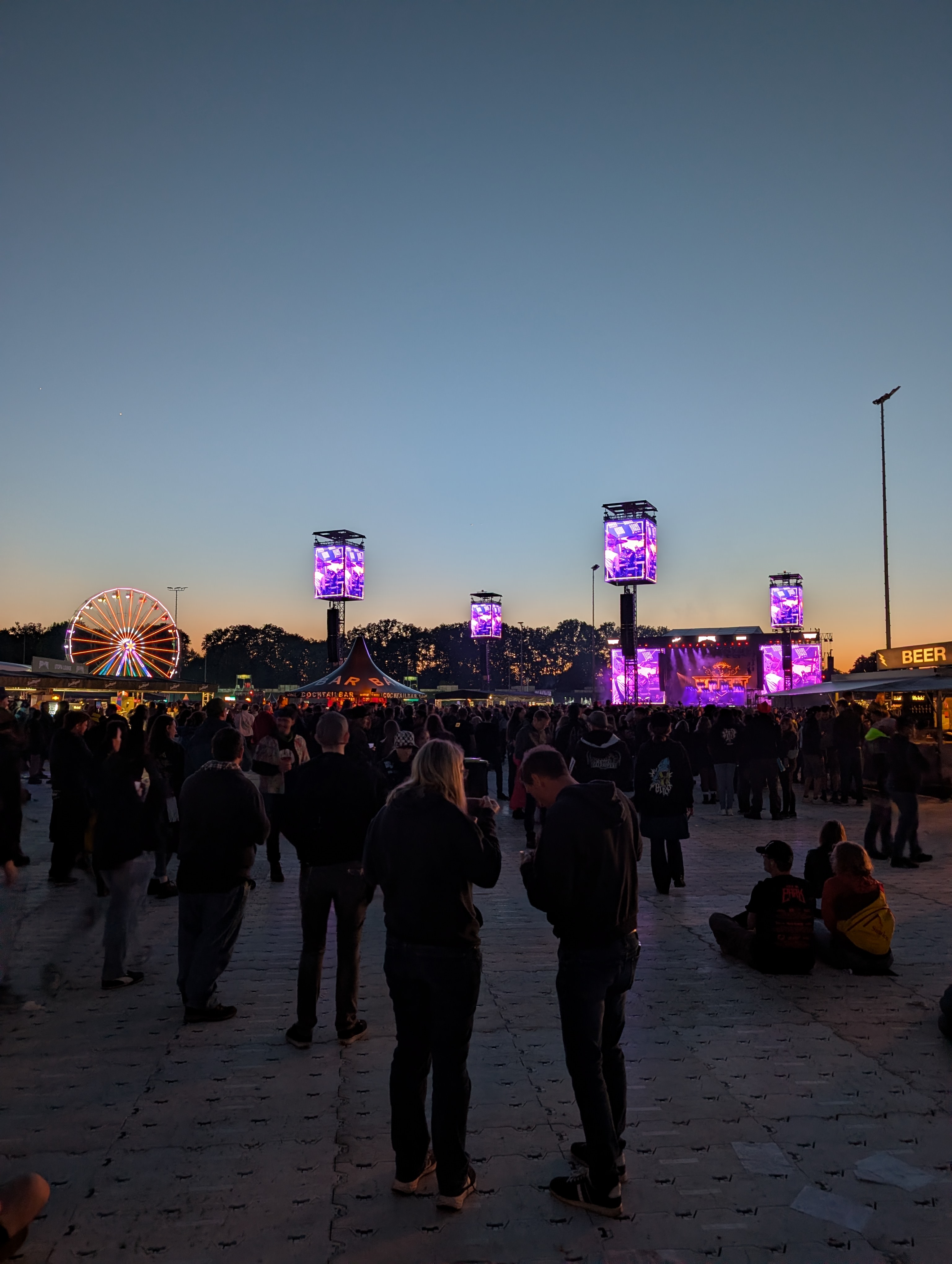 Festivalgelände in der Dämmerung: beleuchtete Bühne, Lichttürme und ein leuchtendes Riesenrad vor tiefblauem Himmel – Aufmacherbild zum Einblick über Musikszenen, Wissen und kreative Infrastruktur.