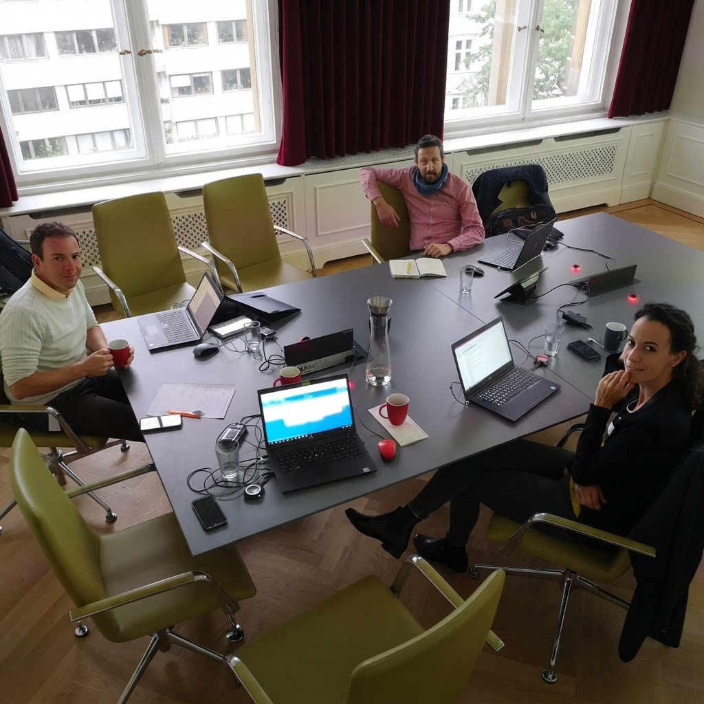 Helles Meetingzimmer mit großem Konferenztisch, Laptops und drei arbeitenden Personen am Tisch – Aufmacherbild zum Einblick über Kreativkompetenz in der Gründungsförderung.