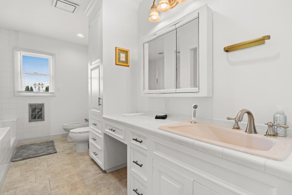 Palmetto Suite all-white bathroom with double vanity, soaking tub, subway tile, gold sconce, and medicine cabinet at Laurel Haven Estate Lancaster SC