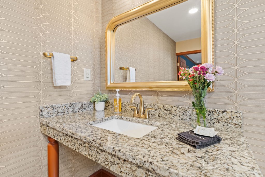 Peacock Suite bathroom with gold ornate mirror, granite countertop, brass faucet, fresh flowers, and geometric tile wall at Laurel Haven Estate