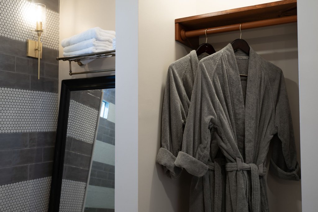 Peacock Suite oversized walk-in shower with penny tile, grey subway tile, brass grab bar, and plush robes in closet at Laurel Haven Estate