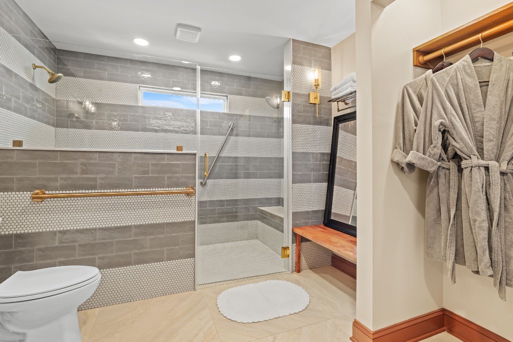Peacock Suite oversized accessible walk-in shower with penny tile, brass grab bar, bench seat, and plush robes at Laurel Haven Estate