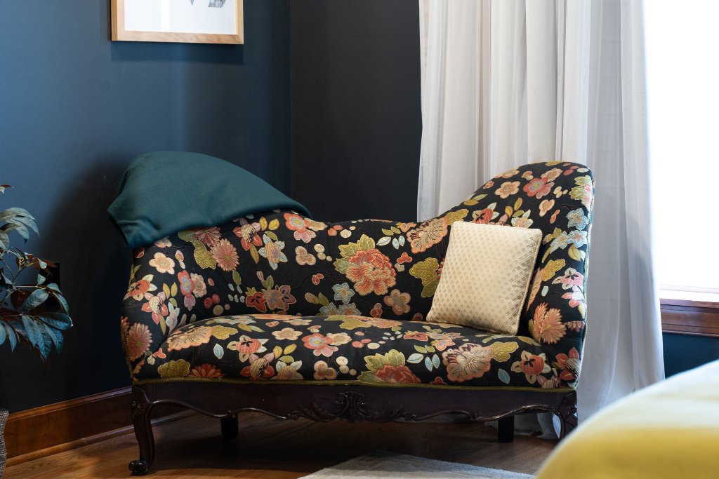 Peacock Suite antique floral settee with teal pillow beside sheer curtained window in charcoal-walled bedroom at Laurel Haven Estate