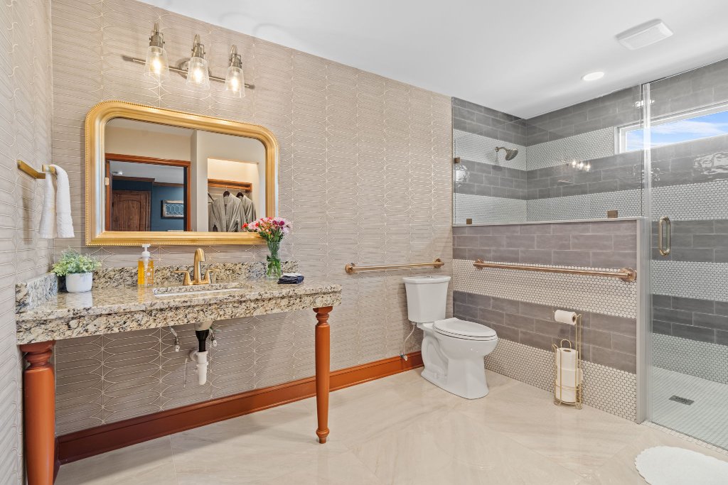 Peacock Suite ADA accessible full bathroom with granite vanity, gold mirror, walk-in shower, grab bars, and geometric tile at Laurel Haven Estate