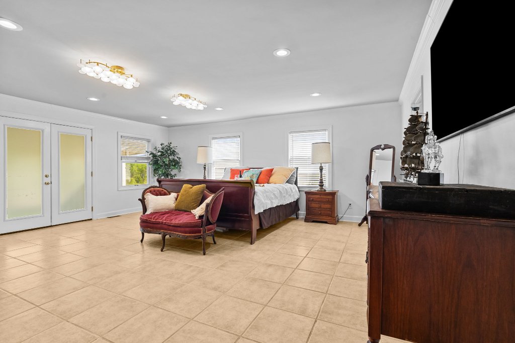 Palmetto Suite king bedroom full view with smart TV, gold chandelier, French doors, velvet chaise, antique dresser, and plant at Laurel Haven Estate