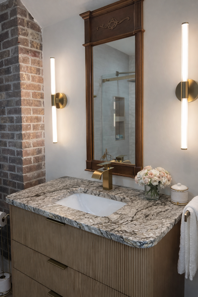 Magnolia Suite bathroom vanity with dramatic granite countertop, brass waterfall faucet, antique mirror, and blush roses at Laurel Haven Estate