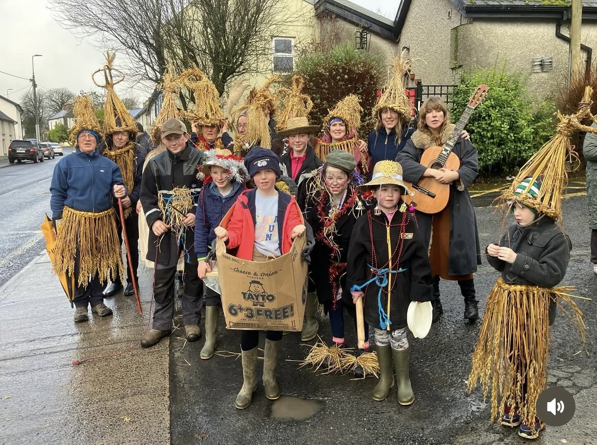Children and adults in straw wren boy costumes on a suburban street
