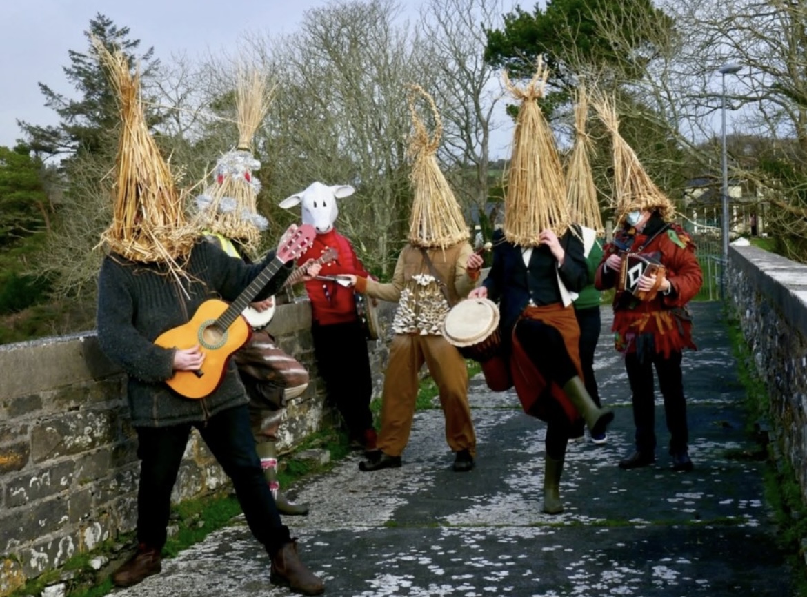 Wren boys in straw masks playing guitar, drum, and accordion