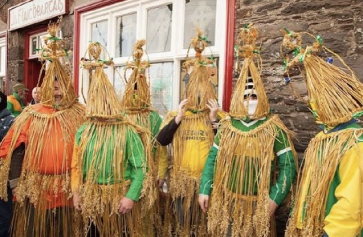 A group of wren boys in conical straw masks in front of a stone building