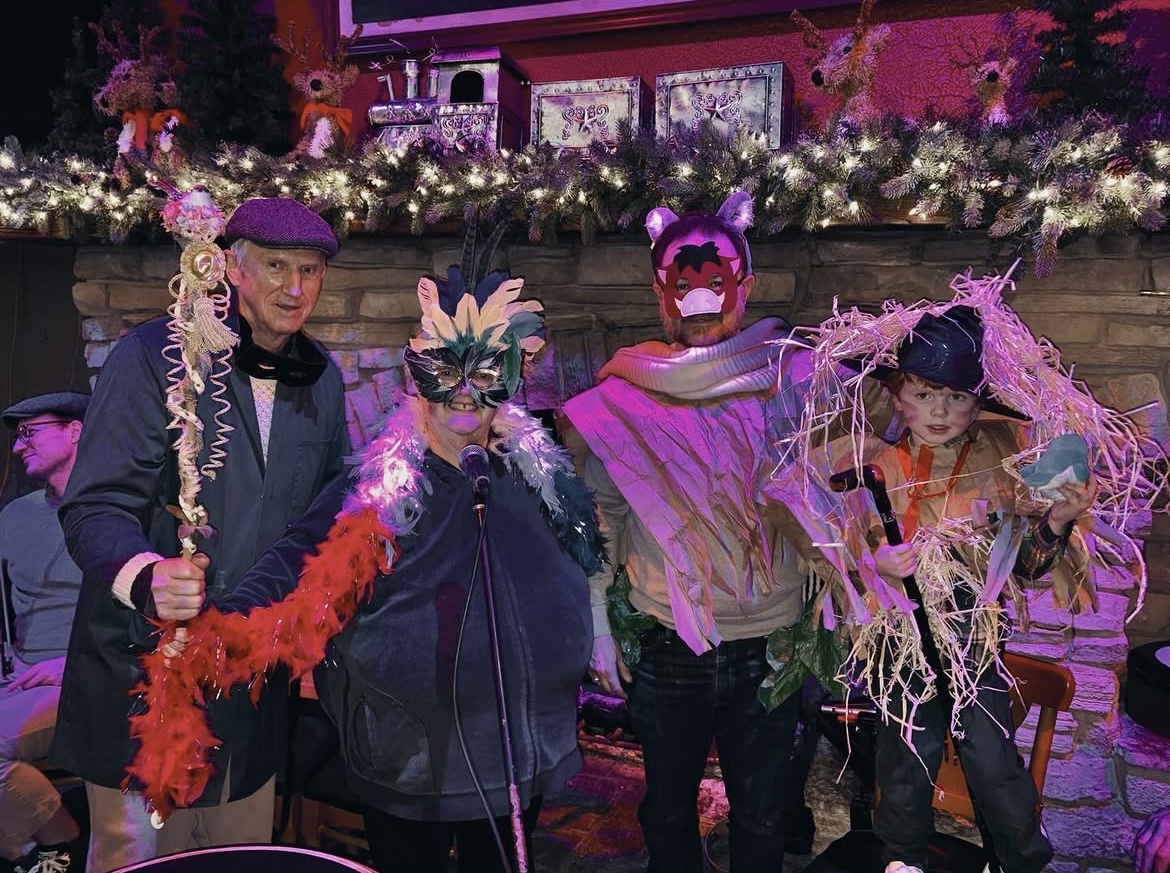 Prize winners in masks, boas, and a straw scarecrow costume in front of a stone fireplace