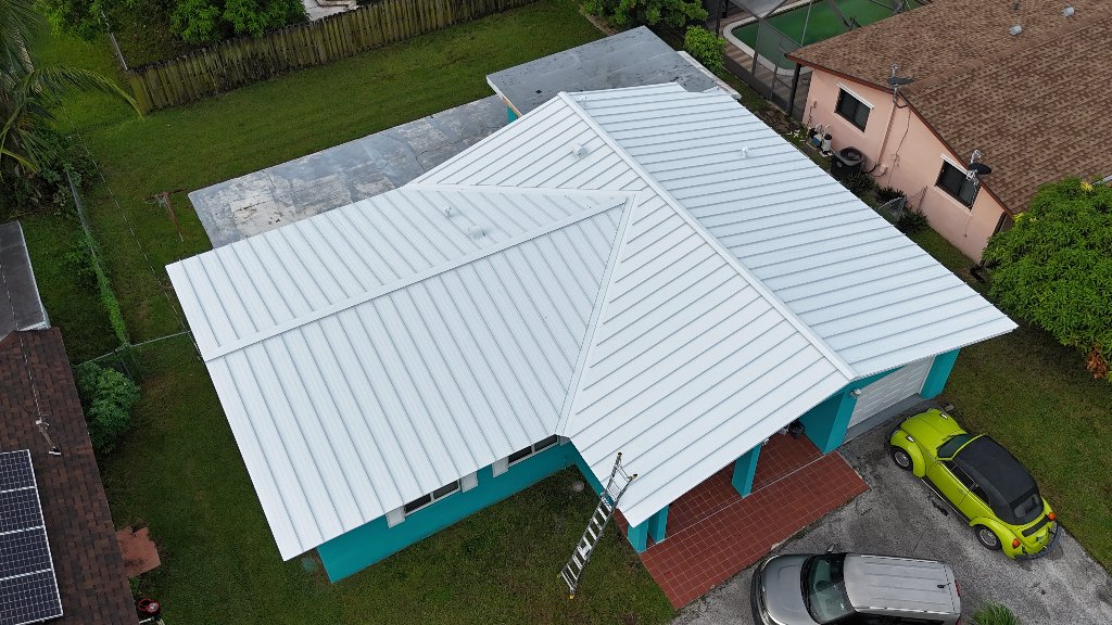 Aerial view of completed white standing seam metal roof replacement on a teal South Florida home