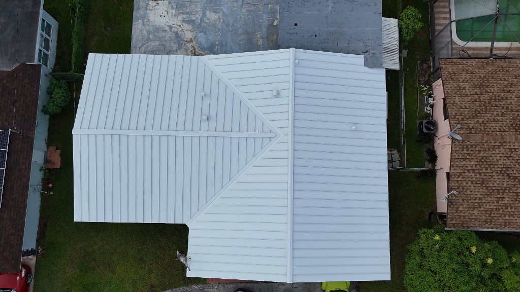 Aerial view of light gray standing seam metal roof with solar panels on a South Florida home