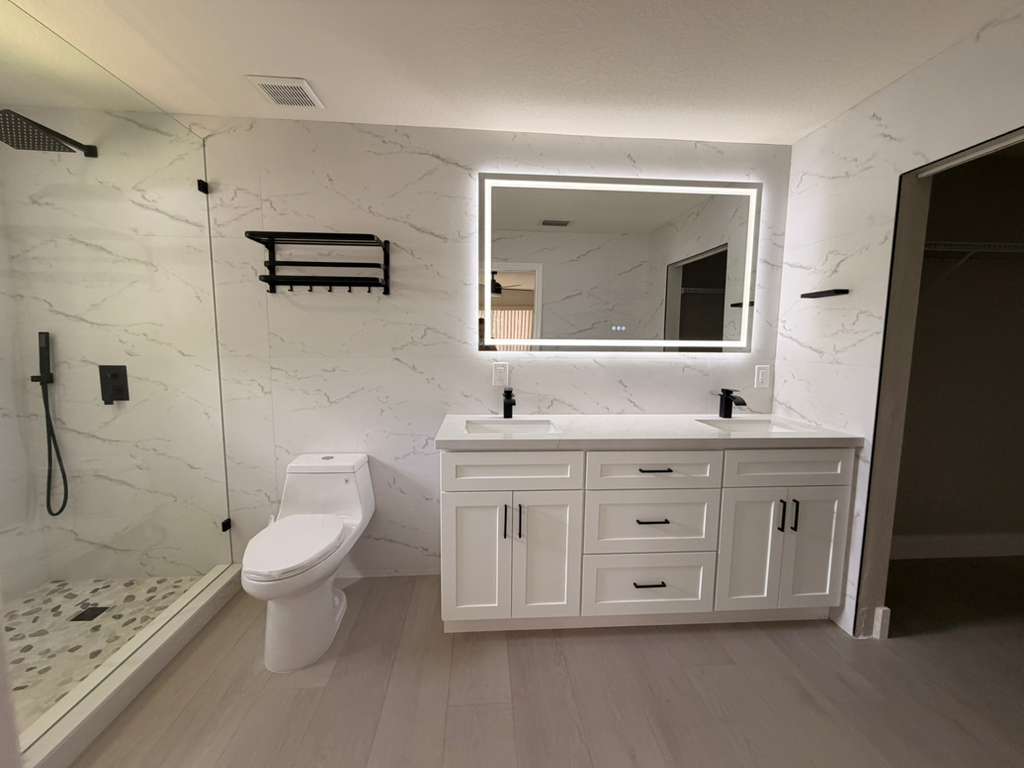 Modern bathroom renovation with white marble-look tile, double vanity, black fixtures, and frameless glass walk-in shower in South Florida
