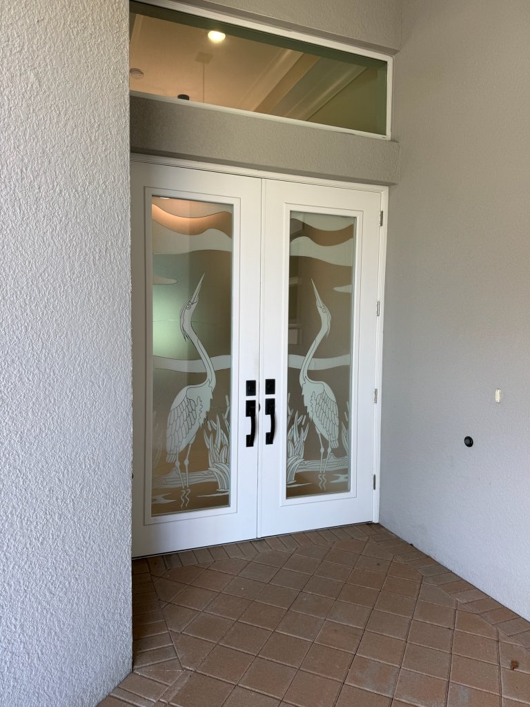 Heron artwork on entry doors beneath a clear transom
