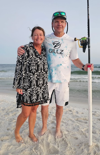 Couple posing with a fishing rod on the beach during an evening shark fishing trip in Gulf Shores, Alabama
